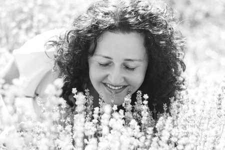 Black and white close-up portrait of curly-haired girl among flowers. Woman closed her eyes and enjoys aroma of lavender. Sincere smile. Digital detox, pleasure from slow life. Soft selective focusの写真素材