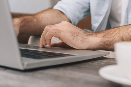Close-up Hands of modern programmer or office manager over laptop keyboard while programming. Guy in blue shirt and white T-shirt. Cup of coffee on table. freelanceの写真素材