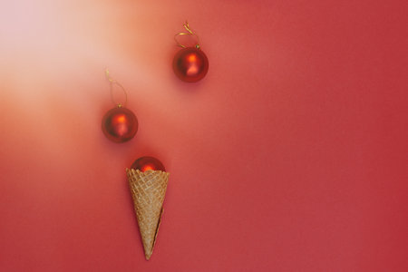 Soft selective focus Christmas balls decoration in waffle cone on red background under bright sun rays. Round toys with gold thread. flat layの写真素材