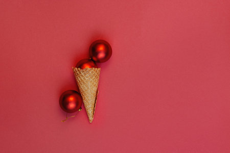 Flat lay Alternative ice cream Christmas balls in waffle cone on red background. One rolled off corner. Winter holiday celebration concept, top view festive composition.の写真素材