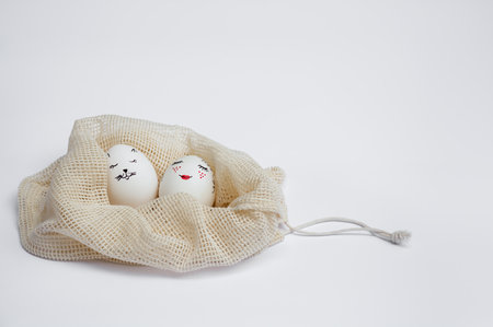 Beautifully painted Easter eggs lie in eco-friendly drawstring mesh bag on white table. Funny spades painted on eggs. copyspace. happy holidaysの写真素材
