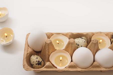 Easter holiday concept. Candlights in eggshell. White chicken and quail eggs in paper tray on white background. creative approach. copy spaceの写真素材