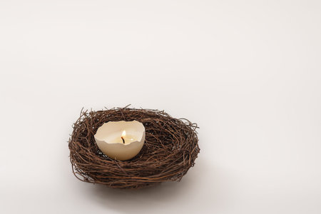 Easter card. Candle in eggshell burns in wicker nest on light background. Preparation for holidays,...