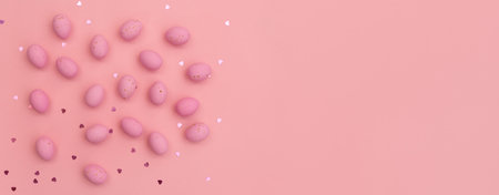 easter greeting card. Banner made from Bright pink chocolate eggs arranged in playful pattern on pastel pink background. Shimmering glowing hearts. Perfect for Easter and spring themes. happy holidaysの写真素材