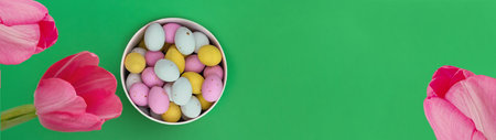 Banner made from Multi Colored chocolate eggs in box and pink tulips on green background. Egg colors: pink, yellow and white. copyspace. Ideal for spring themes, use in marketing materials, packagingの写真素材