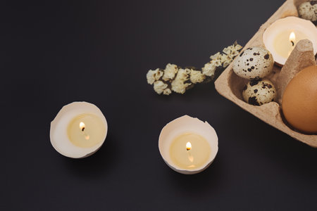 Easter card with candles in eggshell and tray with egg on dark background. white flower. Holiday is made with your own hands. creative approach. copy spaceの写真素材