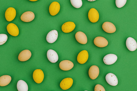 Happy Easter greeting card. Close up Easter candies, chocolate multi colored yellow and white eggs on green background. Flat lay, top view, copy spaceの写真素材