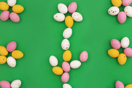 Easter card. Frame of delicious close up chocolate eggs arranged in shape of flowers on green background. Easter sweets. Use for holiday or spring advertising. top view, copy spaceの写真素材