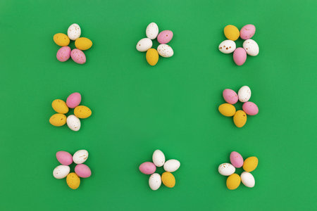Easter background. Colorful chocolate eggs arranged in shape of flowers, which form frame on green background. Use for Easter or spring advertising as decorative image for website. Top view.Copy Spaceの写真素材