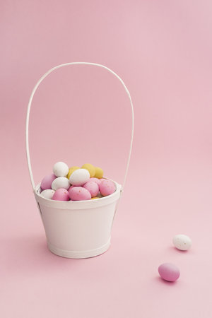 White basket with Easter chocolate multicolored eggs on pastel pink background. Easter composition. Card with Copy Space for textの写真素材