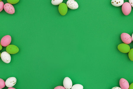 Happy Easter concept. Frame of colorful chocolate eggs arranged in shape of flowers on green background. Use for Easter or spring advertising as a decorative blog image. Flat lay copy spaceの写真素材