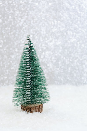 greeting winter card. Green Christmas tree stands among snow on white background. Bright bokeh. Copy space for your designs. Merry Christmasの写真素材