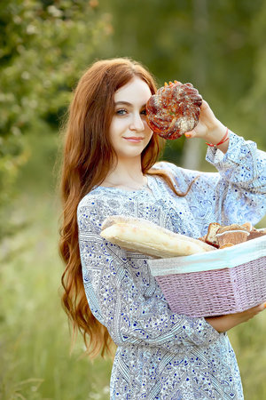 A young girl with blue eyes smiling closed her eyes with a round bagel and holds a basket with homemade cakes on nature. Bakery and bread. food advertising concept.の写真素材