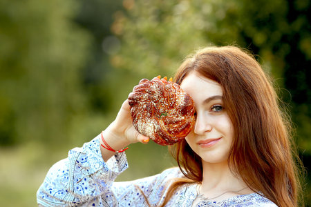 A young girl close-up with blue eyes smiling closed her eyes with a round bagel and holds a basket with homemade cakes on nature. Bakery and bread. food advertising concept. Copy space on the leftの写真素材