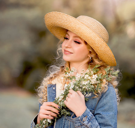 Outdoor portrait of beautiful young woman in straw hat with flowers.の写真素材