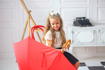 Cute little schoolgirl sitting with a red umbrella on a chair in a room where: table, chair, abacus, books, backpack. education. autumn conceptの写真素材