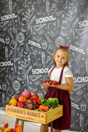 A cute Caucasian girl in a school uniform is studying vegetables in the classroom. elementary school. education concept.の写真素材