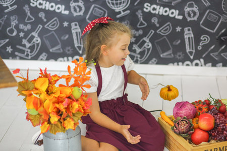 Little cute schoolgirl sitting in the classroom. Study of vegetables and fruits. children. elementary school. education concept.の写真素材