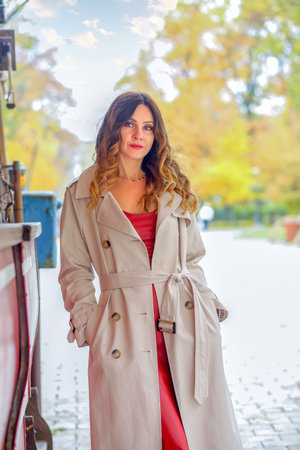 Calm girl in a beige raincoat and red dress walking in the autumn park. autumn conceptの写真素材
