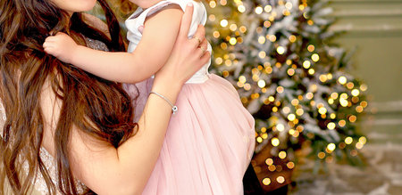 Banner with Mom and little daughter in pink dresses in New Year's interior. Garland and Christmas tree with firelight in the background. Family conceptの写真素材