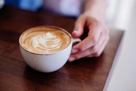 Close up of beautiful female hand holding big white cup of cappuccino coffee.の写真素材