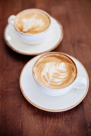 Two cups of cappuccino in white cups on a wooden table in a cafe.の写真素材