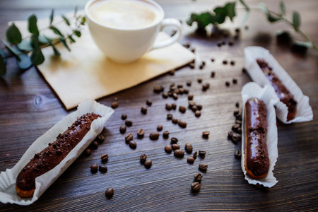 Cup of cappuccino on the wooden table, chocolate eclairs and eucalyptus.