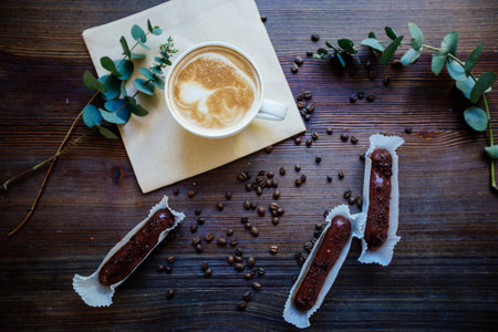 Cup of cappuccino on the wooden table, 
chocolate eclairs and eucalyptus.