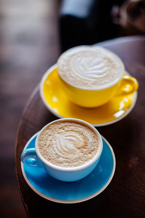 Two cups of cappuccino in color cups on a wooden table in a cafe