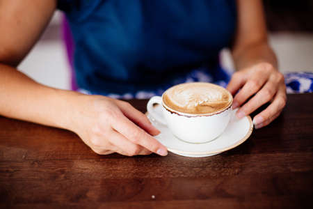 Close up of beautiful female hand holding big white cup of cappuccino coffee.の写真素材