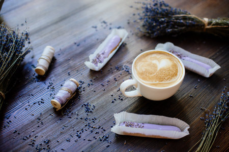 Cup of cappuccino on the wooden table, eclairs and flowers of lavender.