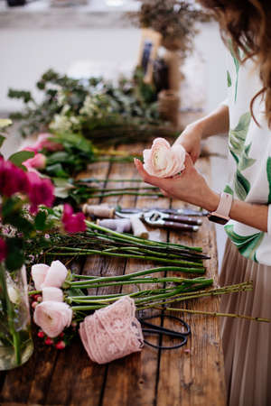 A girl florist makes a bouquet in a light studio on a wooden table.の写真素材