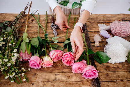 A girl florist makes a bouquet in a light studio on a wooden table.の写真素材