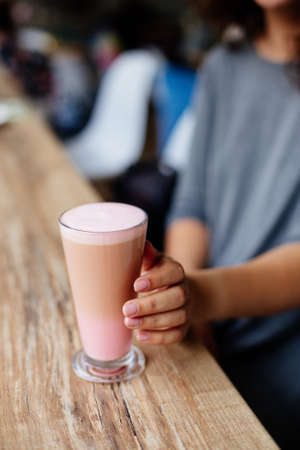 Close up of beautiful female hand holding big cup of pink cappuccino coffeeの写真素材