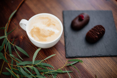 Cup of cappuccino in white cups on a wooden table in a cafe and chocolate candies.