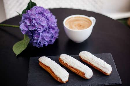 Cup of cappuccino on the black table, eclairs and flowers.の写真素材