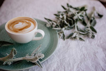 A cup of cappuccino and flowers on a wooden table.の写真素材
