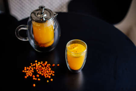 Vitaminic healthy sea buckthorn tea in small glass tea pot with fresh raw sea buckthorn berries.の写真素材