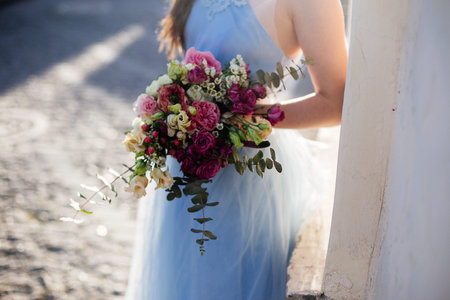 Beautiful girl bride in a blue dress with long hair at sunset holding a beautiful bouquet.の写真素材