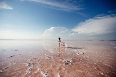 Beautiful woman on a pink salty lake. Beautiful figure. Reflection in water.の写真素材