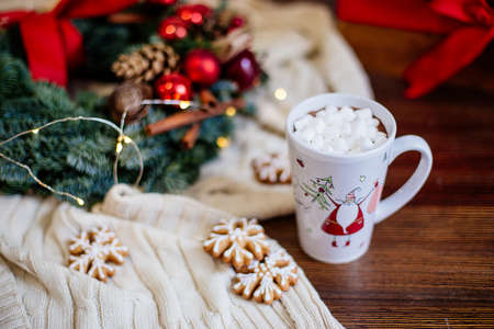 Christmas wreath of fir branches with red decor and a cup of cocoa with marshmallows on a wooden table. New Year and Christmas concept.の写真素材