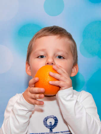 Child Emotions. Funny boy. A boy with blue eyes. Portrait. The orange in his hands.の写真素材