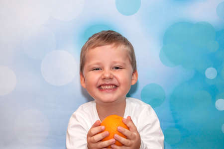 Child Emotions. Funny boy. A boy with blue eyes. Portrait. The orange in his hands.の写真素材