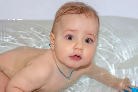 The child is bathing in the bath. Games in the water. Bathing a child. Toys in the bathroom. Portrait of a babyの写真素材