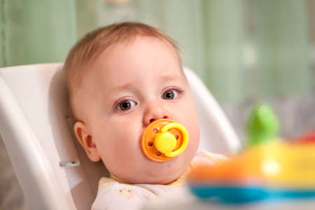 A baby in a high chair playing with toys. The pacifier in his mouth.の写真素材