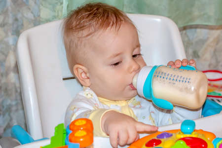 A baby in a high chair playing with toys. Eats a mixture from a bottle.の写真素材