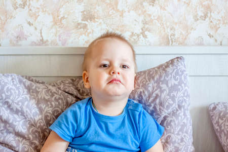 A sad child is lying in bed. Emotions of children. The baby has a cold.の写真素材
