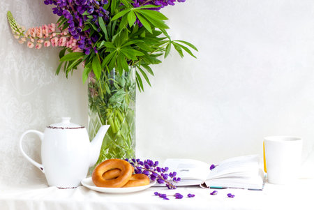 Sweet bagels and tender lupine flowers. Light composition with bright and purple flowers. A gentle and romantic morning with tea and a book. A book of poems for Breakfast.の写真素材