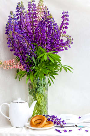 Sweet bagels and tender lupine flowers. Light composition with bright and purple flowers. A gentle and romantic morning with tea and a book. A book of poems for Breakfast.の写真素材