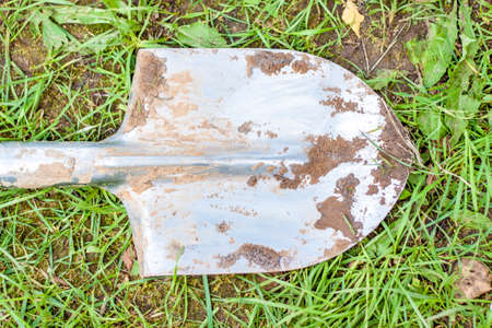 A dirty shovel is lying on the grass after work. Metal shovel. Mud Tools for working in land management.の写真素材